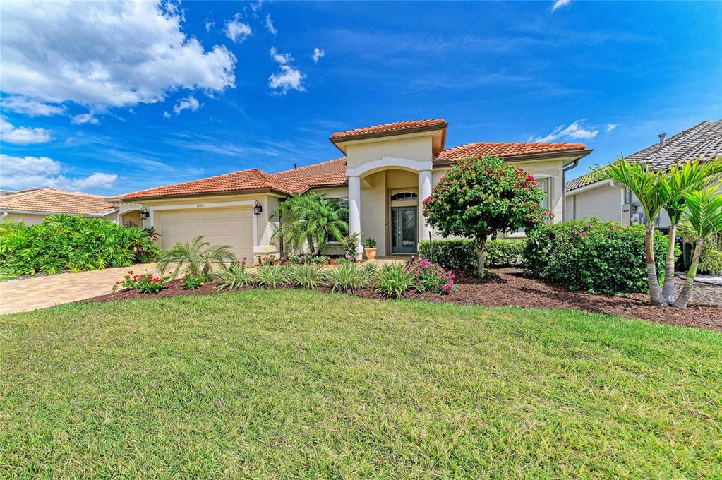 A single-story house with a tile roof, beige stucco exterior, and a landscaped front yard — 1920 COCONUT PALM CIRCLE, NORTH PORT, FL