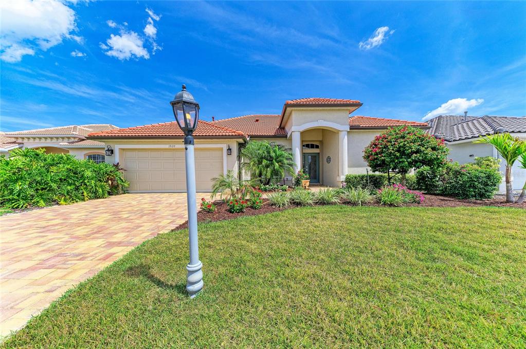 A single-story house with a tan stucco exterior, a tile roof, and a paved driveway — 1920 COCONUT PALM CIRCLE, NORTH PORT, FL