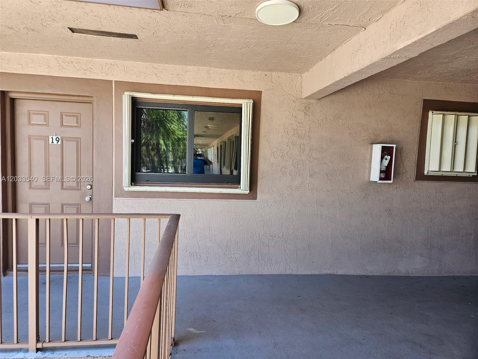 An exterior view of a building corridor featuring a door numbered 19 and a window — 2348 W 56th St # 19, Hialeah FL 33016, HIALEAH, FL
