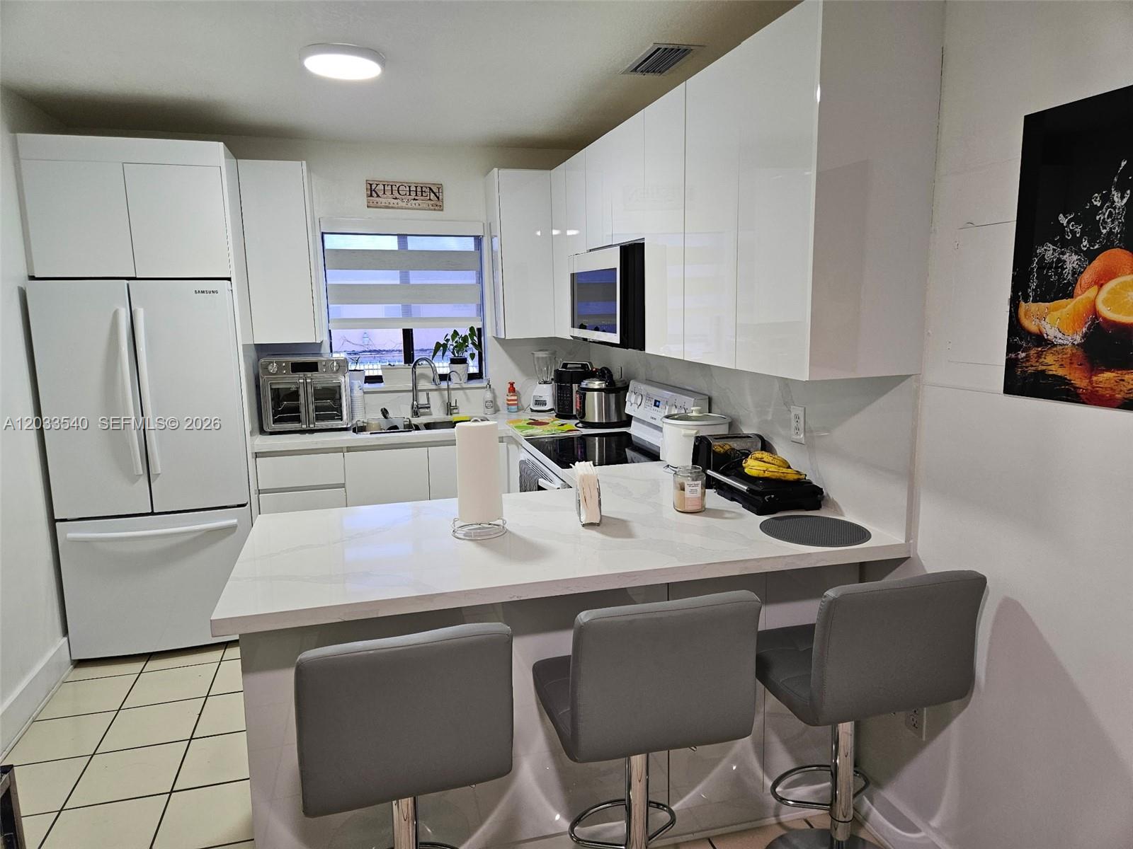 A modern kitchen features white glossy cabinets, a quartz countertop, and three grey bar stools — 2348 W 56th St # 19, Hialeah FL 33016, HIALEAH, FL