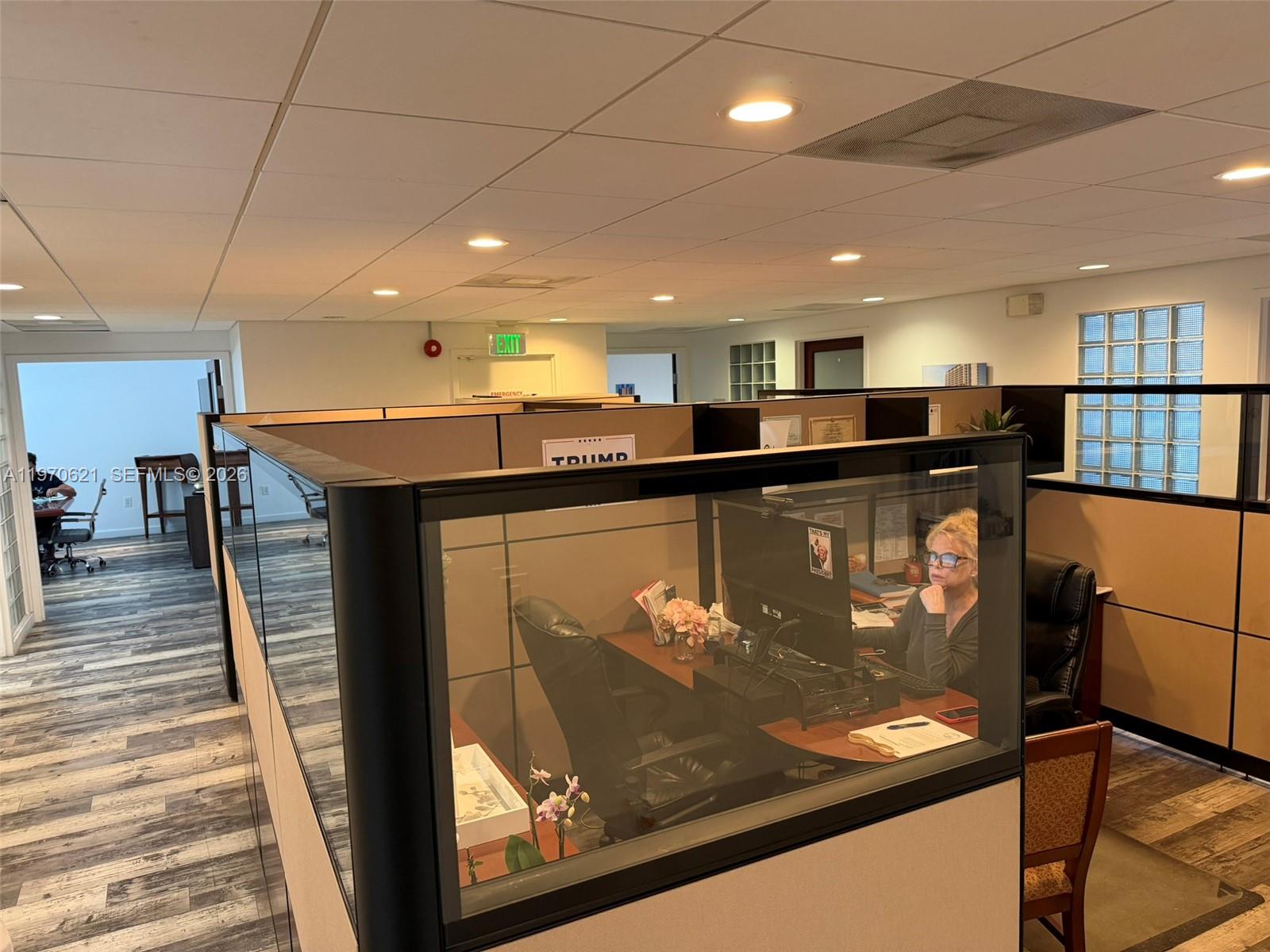An office interior features cubicles with glass partitions, wood-look flooring, and recessed ceiling lights — 2650 SW 27th Ave, Miami FL 33133, MIAMI, FL