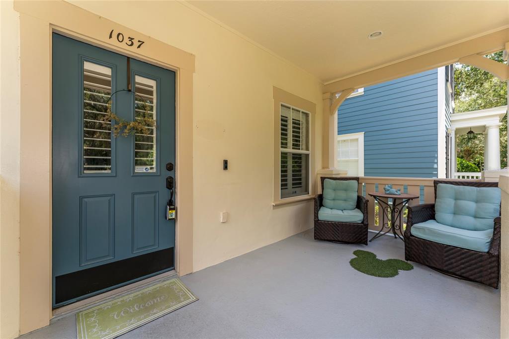 A covered front porch features a blue door, two wicker chairs, and a small table — 1037 OLD BLUSH RD, CELEBRATION, FL