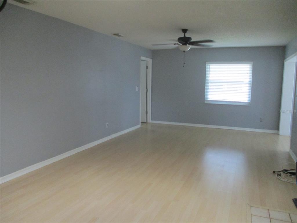 A living room with light-colored wood flooring, gray walls, a ceiling fan, and a window — 2124 HAILSTONE CIRCLE, SUN CITY CENTER, FL