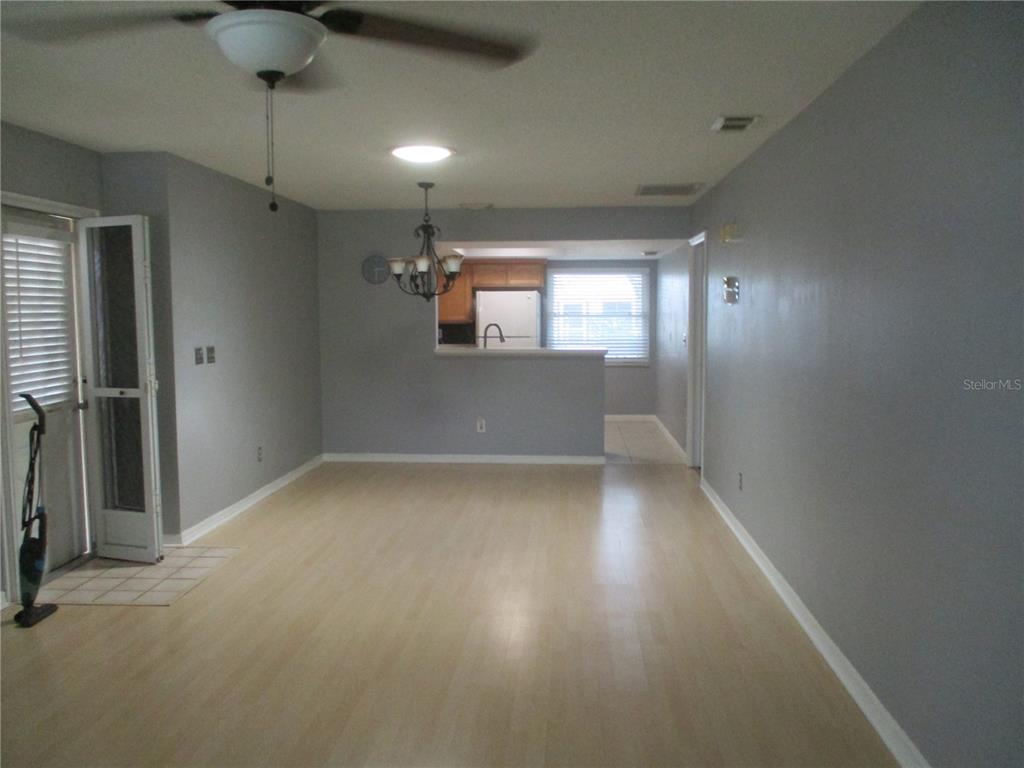 A living room with light wood flooring, gray walls, a ceiling fan, and a kitchen pass-through — 2124 HAILSTONE CIRCLE, SUN CITY CENTER, FL