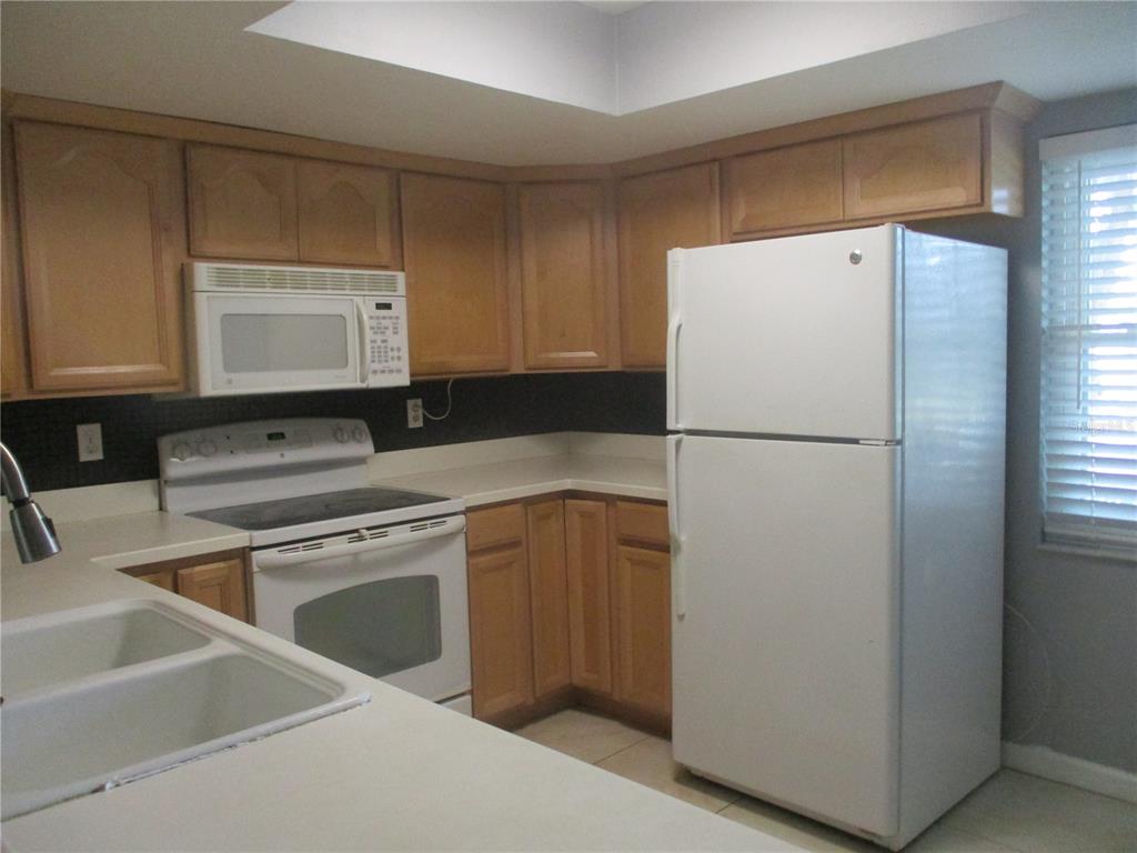 A kitchen features light wood cabinets, white appliances, and a white countertop — 2124 HAILSTONE CIRCLE, SUN CITY CENTER, FL