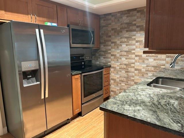 A kitchen features stainless steel appliances, wood cabinets, a stone backsplash, and granite countertops — 7102 W COUNTRY CLUB DRIVE N, SARASOTA, FL