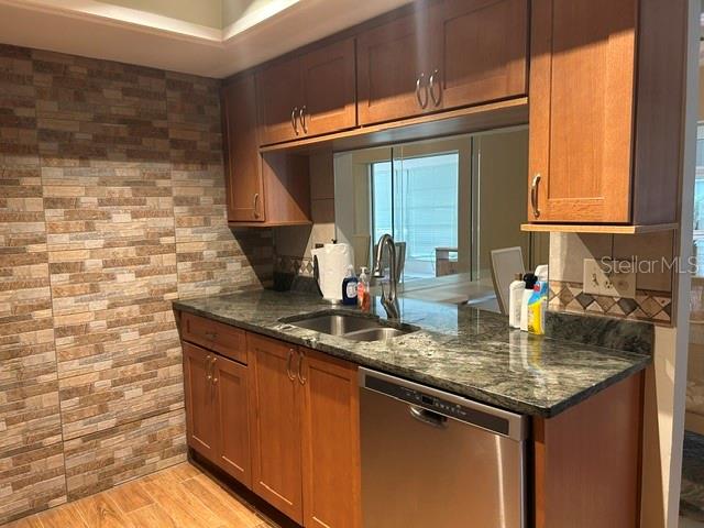 A kitchen features wood cabinets, dark granite countertops, a stainless steel dishwasher, and stone-tiled walls — 7102 W COUNTRY CLUB DRIVE N, SARASOTA, FL