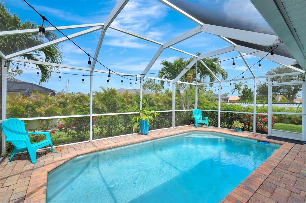 A screened-in patio features a small rectangular swimming pool, brick pavers, and two blue chairs — 28 SW 21ST AVENUE, CAPE CORAL, FL