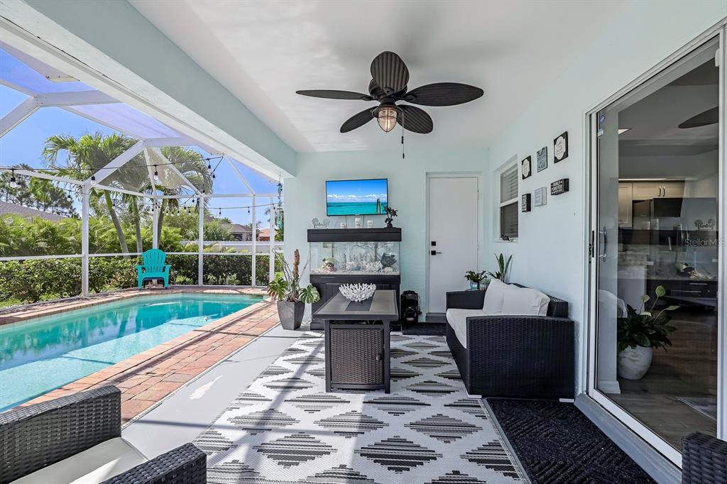 A covered patio features a swimming pool, outdoor furniture, a ceiling fan, and a television — 28 SW 21ST AVENUE, CAPE CORAL, FL