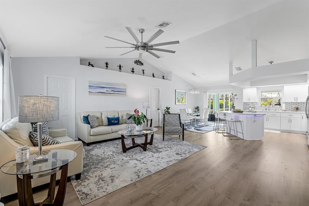 An open-concept living room and kitchen feature vaulted ceilings, light wood flooring, and neutral furniture — 28 SW 21ST AVENUE, CAPE CORAL, FL