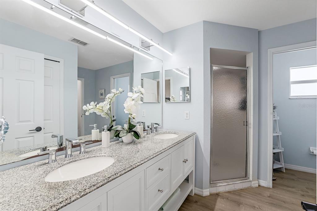 A bathroom with a double vanity, granite countertops, white cabinets, and a glass-enclosed shower — 28 SW 21ST AVENUE, CAPE CORAL, FL