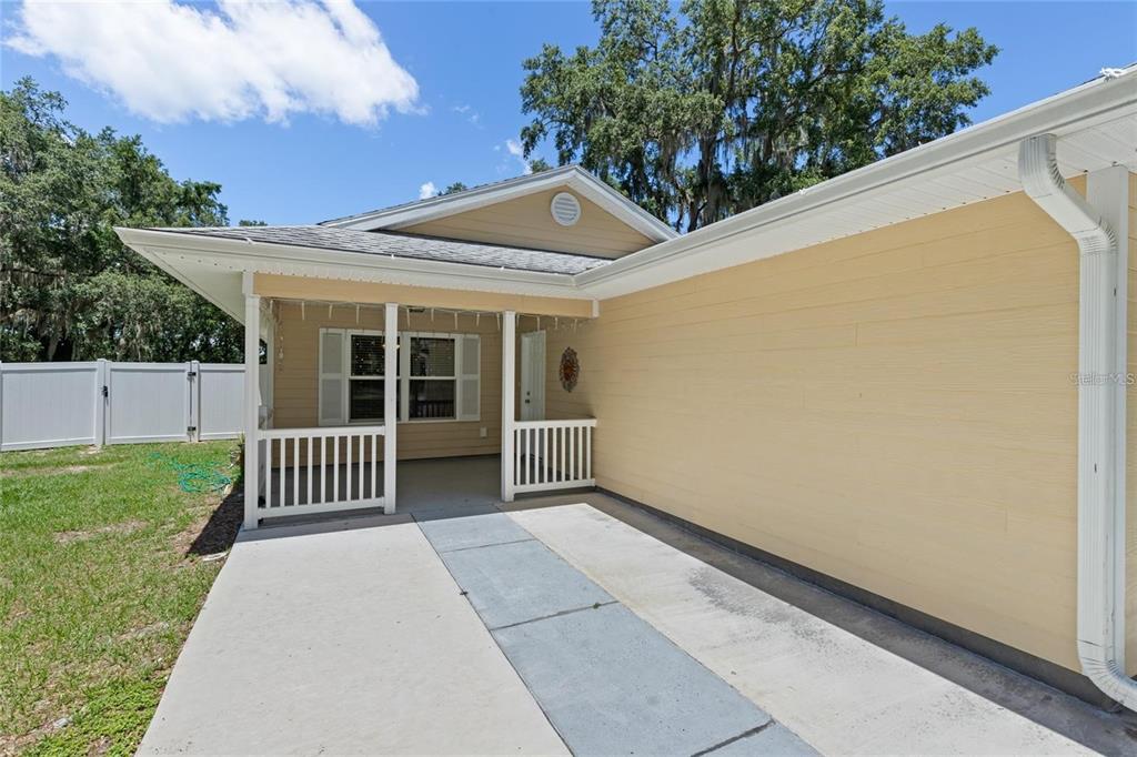 A tan house exterior features a covered porch with white railings and a concrete walkway — 206 E CATAWBA, FRUITLAND PARK, FL