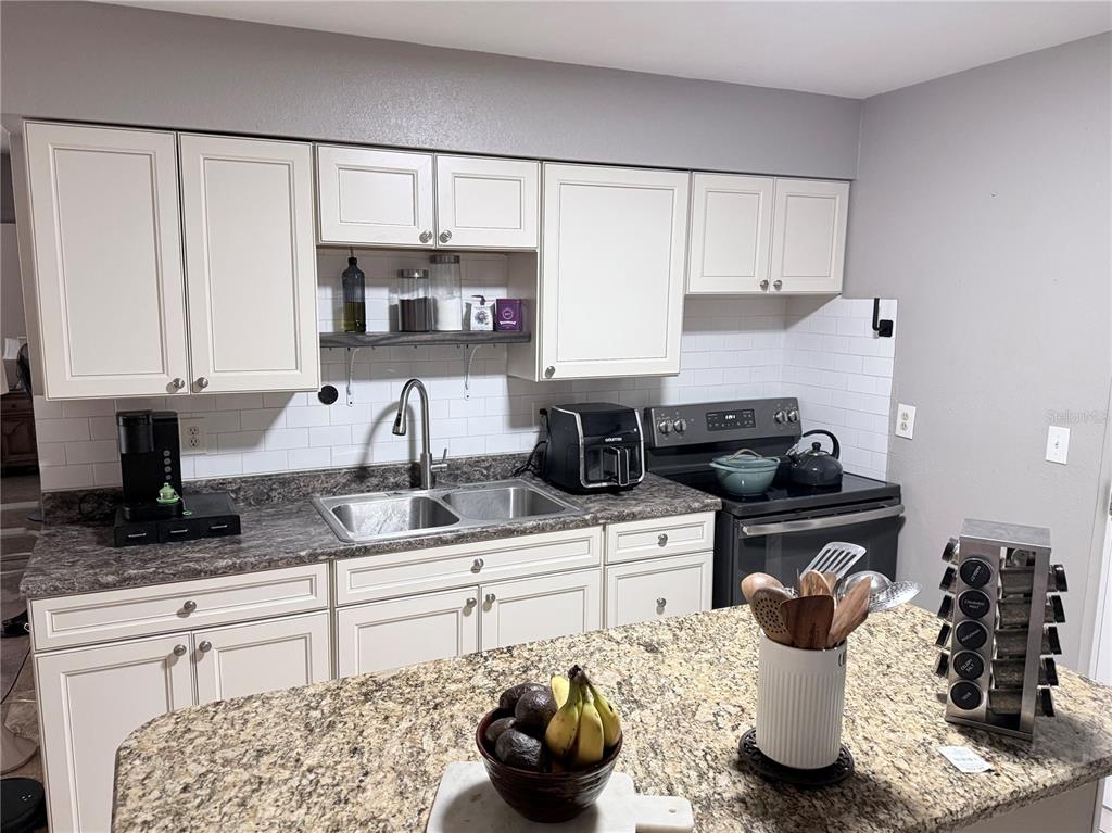 A kitchen features white cabinets, a granite countertop, a double sink, and a subway tile backsplash — 1420 BELLEVIEW ROAD, COCOA, FL