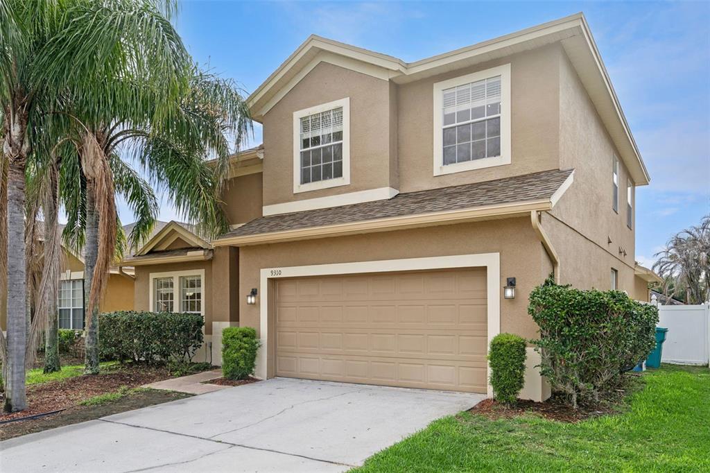 A two-story tan stucco house with a two-car garage and a palm tree — 9310 MUSTARD LEAF DRIVE, ORLANDO, FL