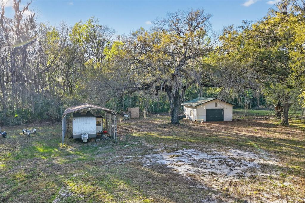 A yard features a metal carport with a camper, a detached garage, and large trees — 1721 COUNTY ROAD 25A, LEESBURG, FL