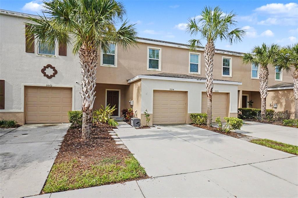A row of tan townhouses features beige garage doors, palm trees, and concrete driveways — 9974 HOUND CHASE DRIVE, GIBSONTON, FL