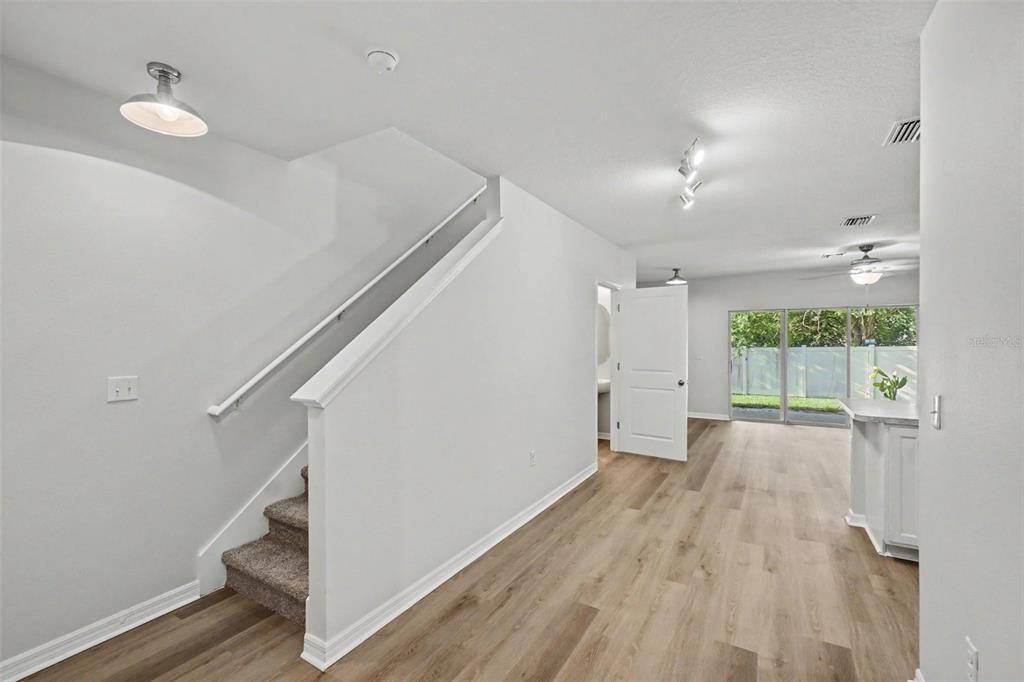 A bright interior space features light wood flooring, a carpeted staircase, and a sliding glass door — 9974 HOUND CHASE DRIVE, GIBSONTON, FL