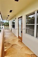 An outdoor walkway with stone-patterned flooring leads to a door and windows along a building — 198 E Mansfield  E # 198, Boca Raton FL 33434, BOCA RATON, FL