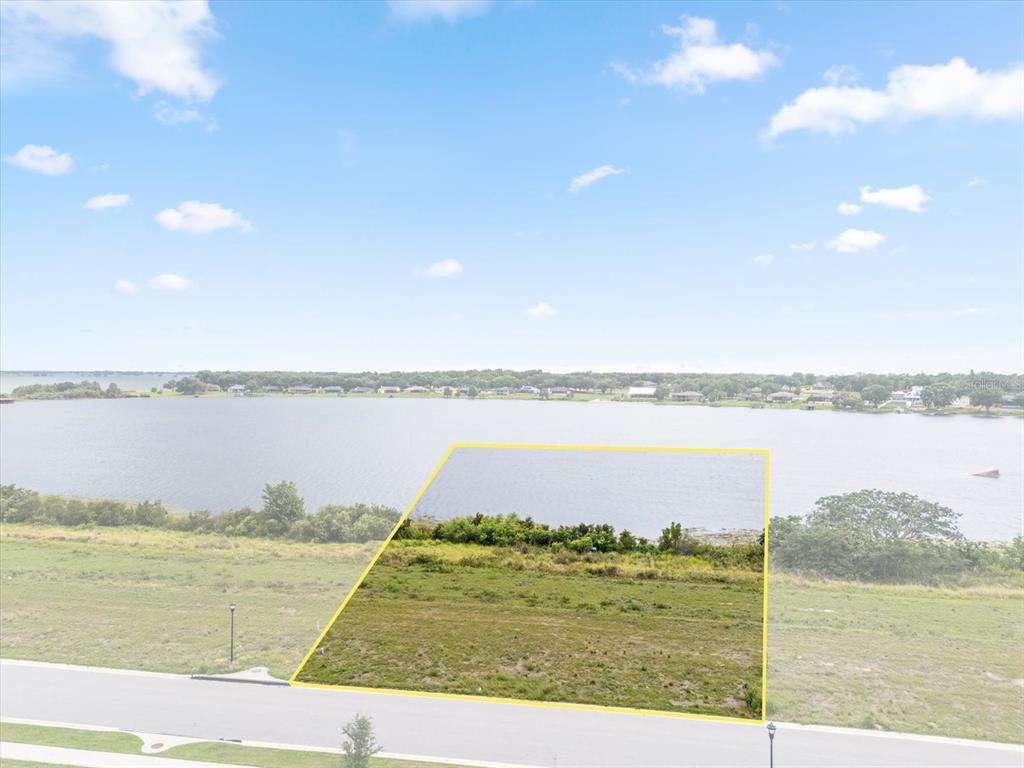 An aerial view shows a vacant, rectangular waterfront lot outlined in yellow near a road — 4343 JULIANA LAKE DRIVE, AUBURNDALE, FL