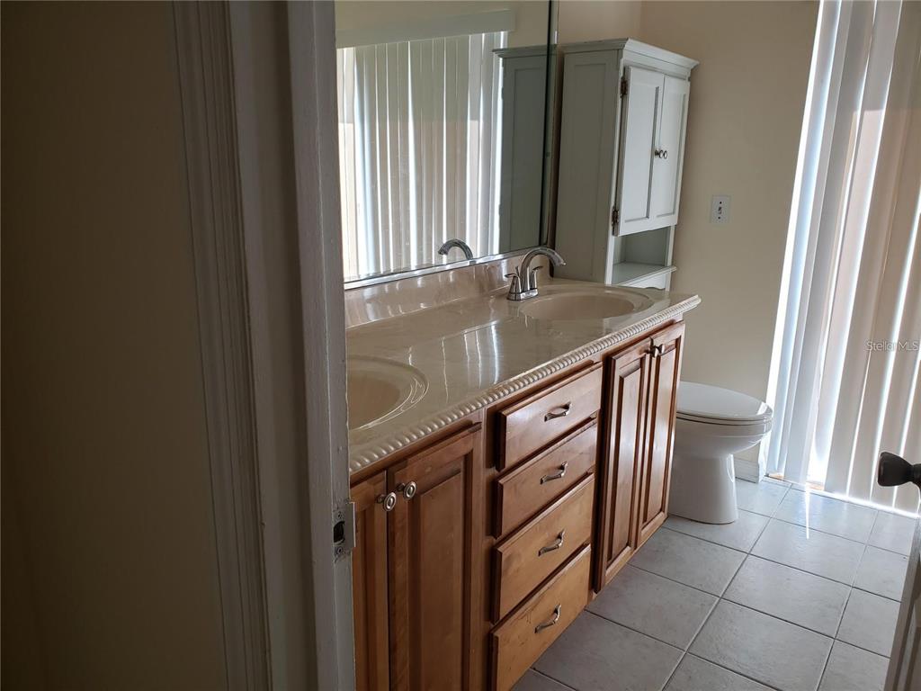 A bathroom features a double-sink vanity with wood cabinets, a large mirror, and tile flooring — 3792 DUNWICH AVENUE, ORLANDO, FL