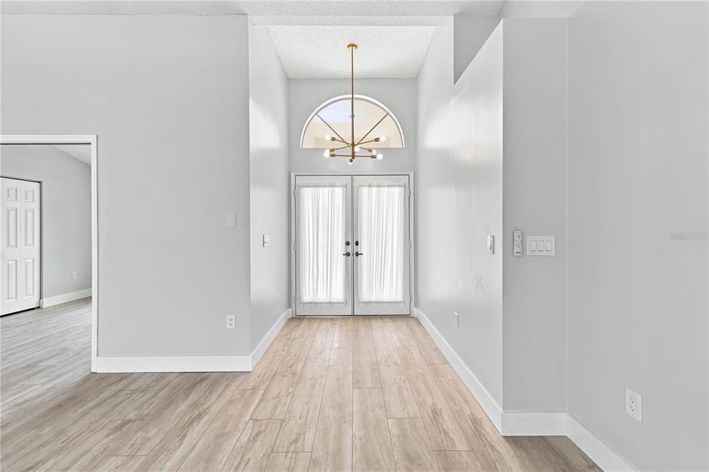 An entryway features light wood-look flooring, a double-door entrance, and a modern chandelier — 5098 WINTERVILLE ROAD, SPRING HILL, FL