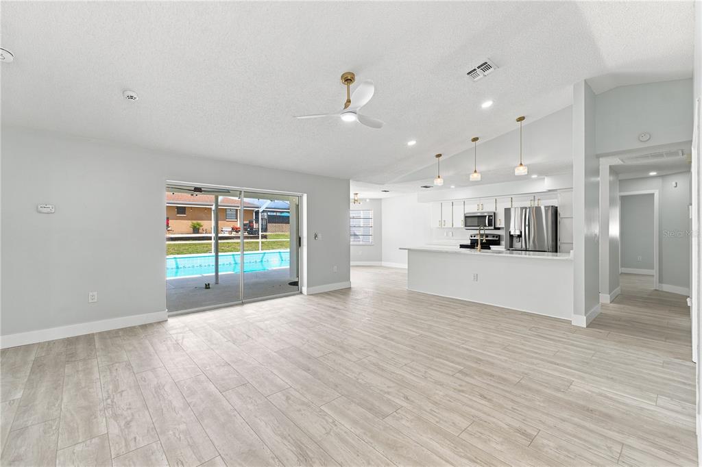 An open-concept living area with light wood-look flooring, a kitchen island, and sliding glass doors — 5098 WINTERVILLE ROAD, SPRING HILL, FL