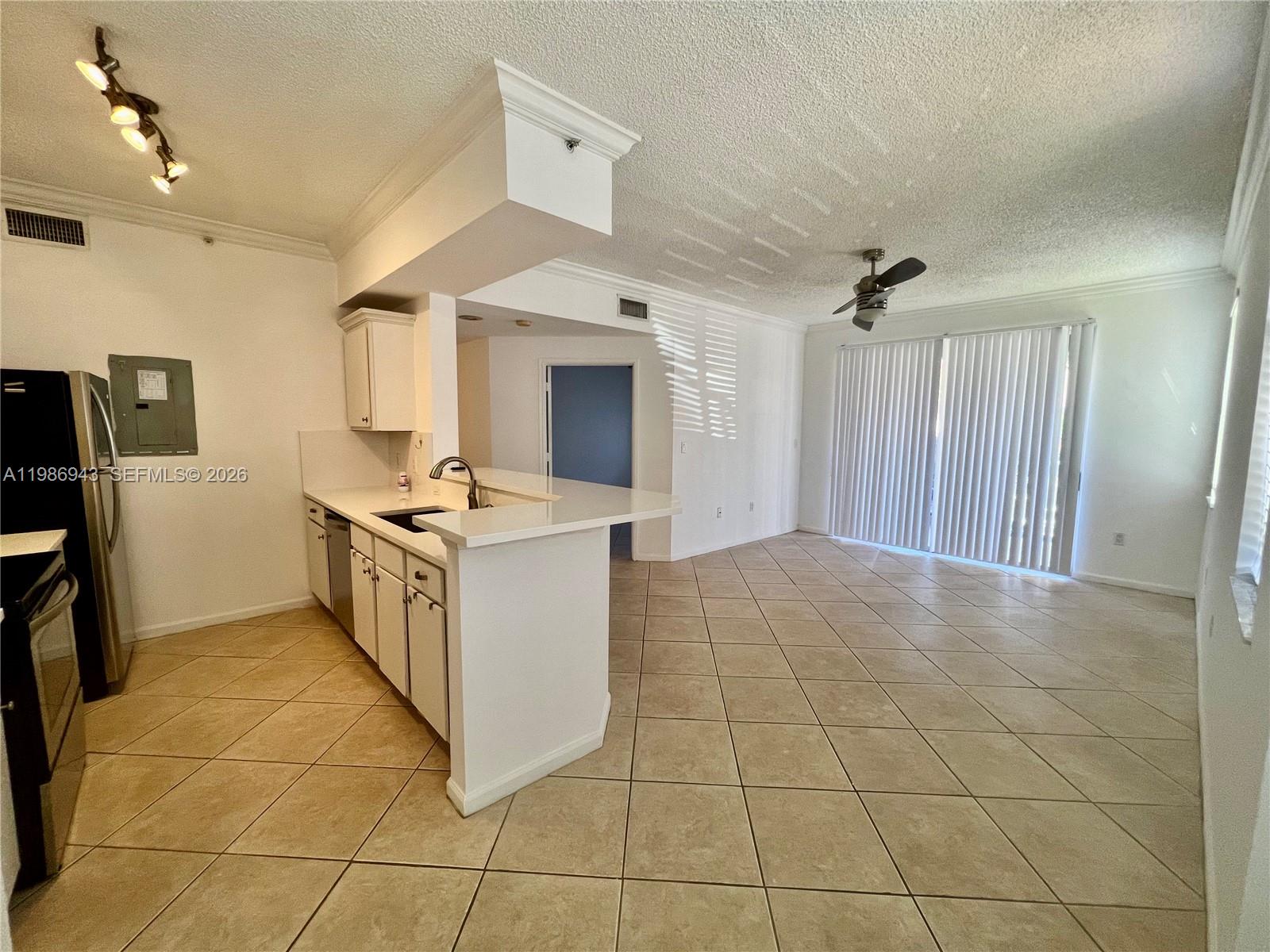 A kitchen with white cabinets and a breakfast bar opens into a tiled living area — 1000 Scotia Dr # 101, Hypoluxo FL 33462, HYPOLUXO, FL
