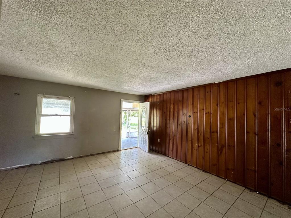 A room with tiled flooring, a popcorn ceiling, wood paneling, and an open exterior door — 4640 NE CUBITIS AVENUE, ARCADIA, FL