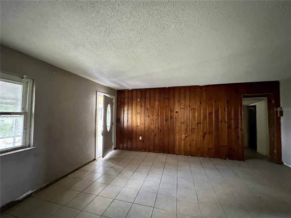 A room with tile flooring, a wood-paneled accent wall, and a white entry door — 4640 NE CUBITIS AVENUE, ARCADIA, FL