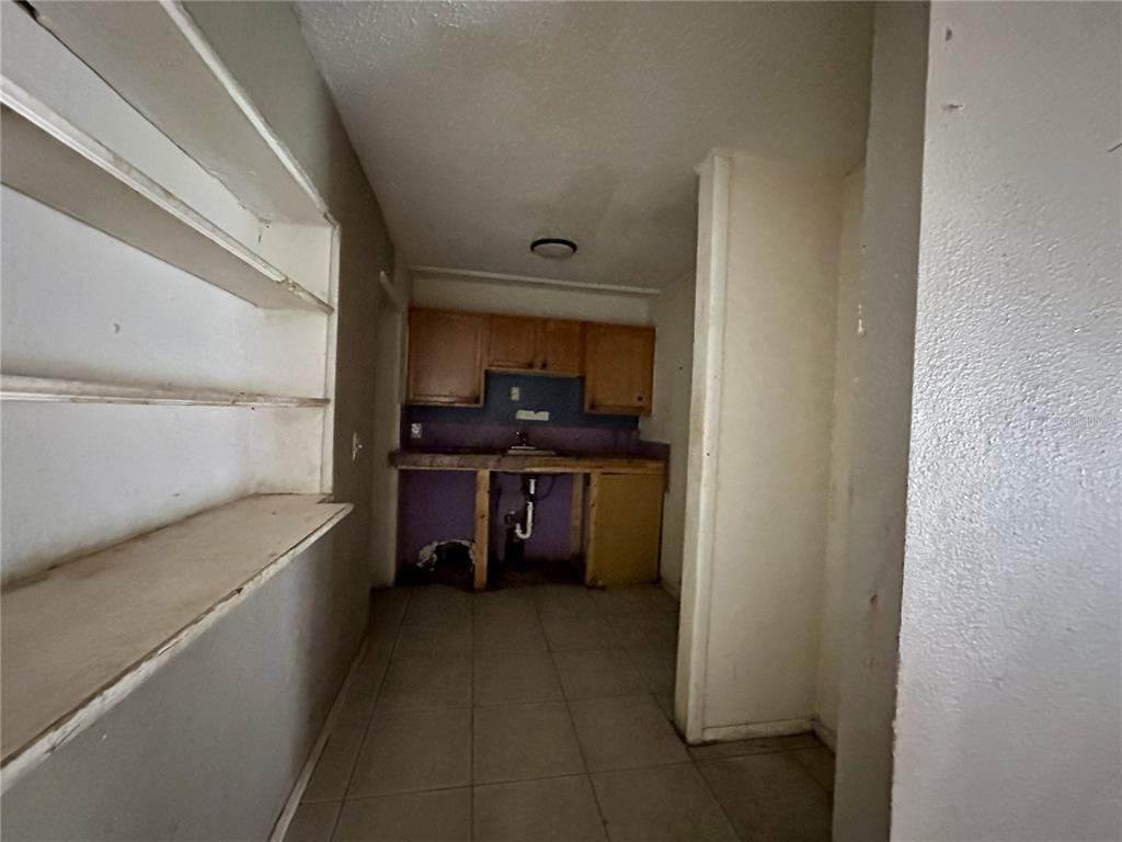 A small, unfinished kitchen features wooden cabinets, open shelving, and tiled flooring — 4640 NE CUBITIS AVENUE, ARCADIA, FL