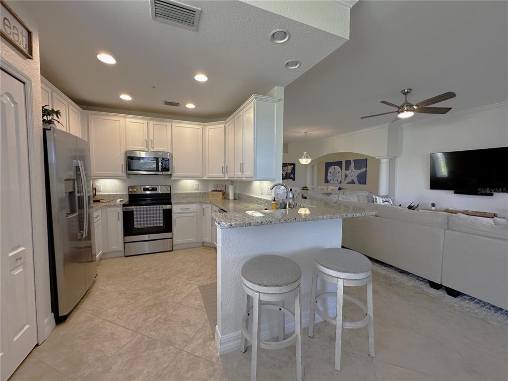 A kitchen with white cabinets, granite countertops, and a breakfast bar with two stools — 14073 BLACK BEAUTY DRIVE UNIT 1012, PUNTA GORDA, FL