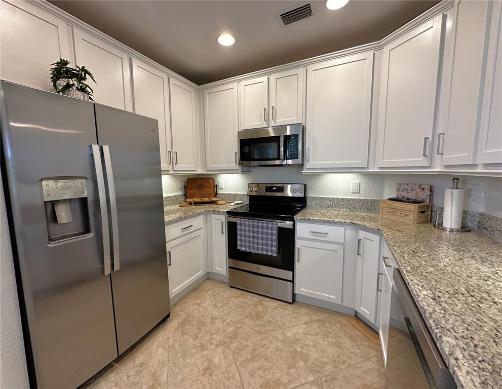 A kitchen features white cabinets, stainless steel appliances, and granite countertops with tile flooring — 14073 BLACK BEAUTY DRIVE UNIT 1012, PUNTA GORDA, FL