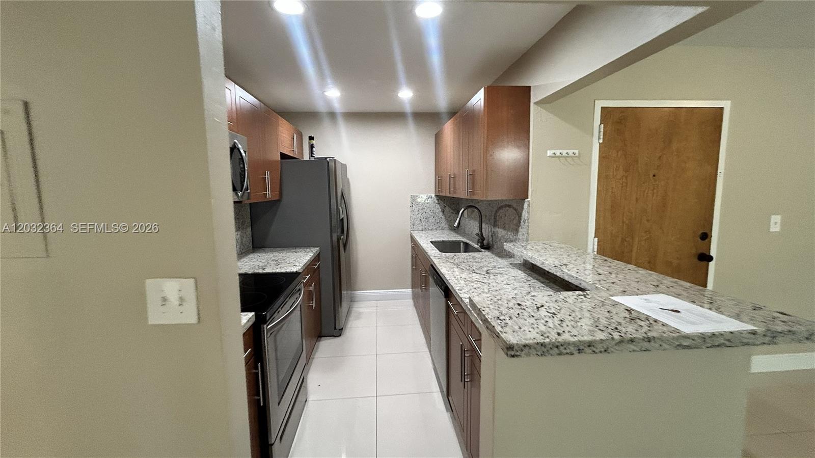 A galley-style kitchen features wood cabinets, granite countertops, and stainless steel appliances — 10377 N Kendall Dr # K8, Miami FL 33176, MIAMI, FL