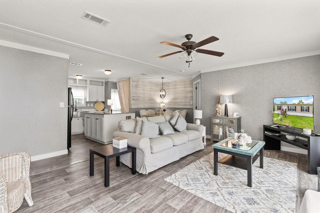 This open-concept living room features gray wood-look flooring, a ceiling fan, and an adjacent kitchen — 6544 W MAE, HOMOSASSA, FL