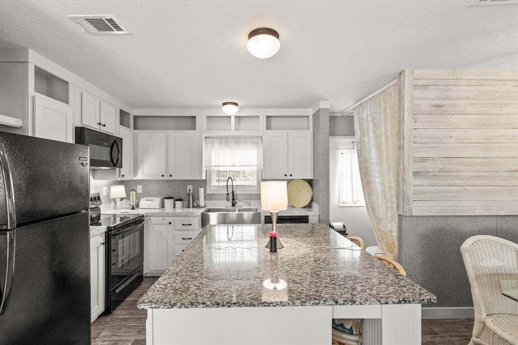 A kitchen features white cabinets, a granite-topped island, black appliances, and a wood-paneled wall — 6544 W MAE, HOMOSASSA, FL