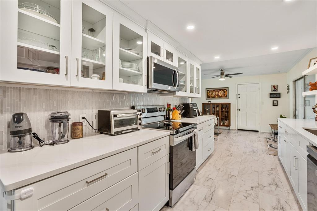 A galley kitchen features white cabinets, quartz countertops, a tiled backsplash, and marble-look floor tiles — 2464 LYDIA WAY, NEW SMYRNA BEACH, FL
