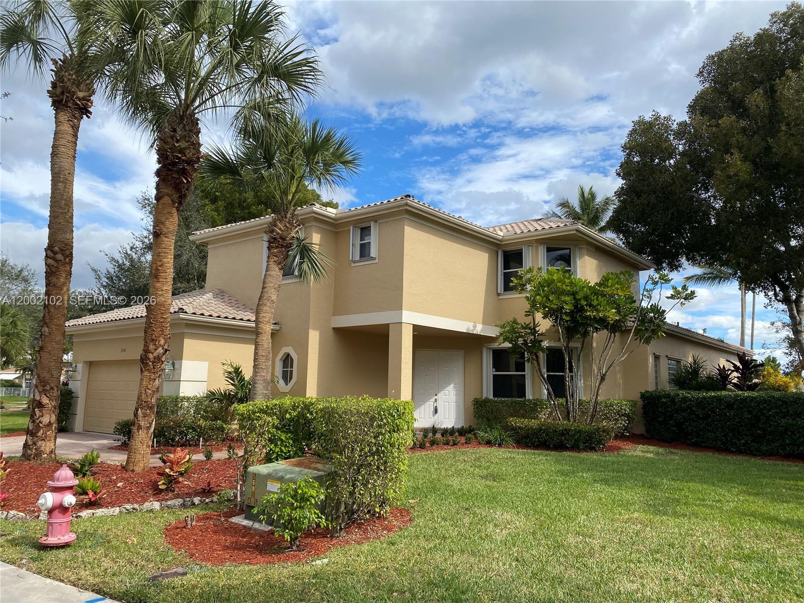 A two-story tan stucco house features a tile roof, palm trees, and a front lawn — 2486 Bay Isle Dr, Weston FL 33327, WESTON, FL