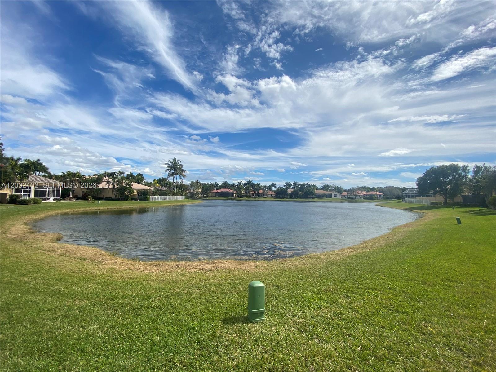 A view of a lake surrounded by grassy lawns and residential houses under a cloudy sky — 2486 Bay Isle Dr, Weston FL 33327, WESTON, FL