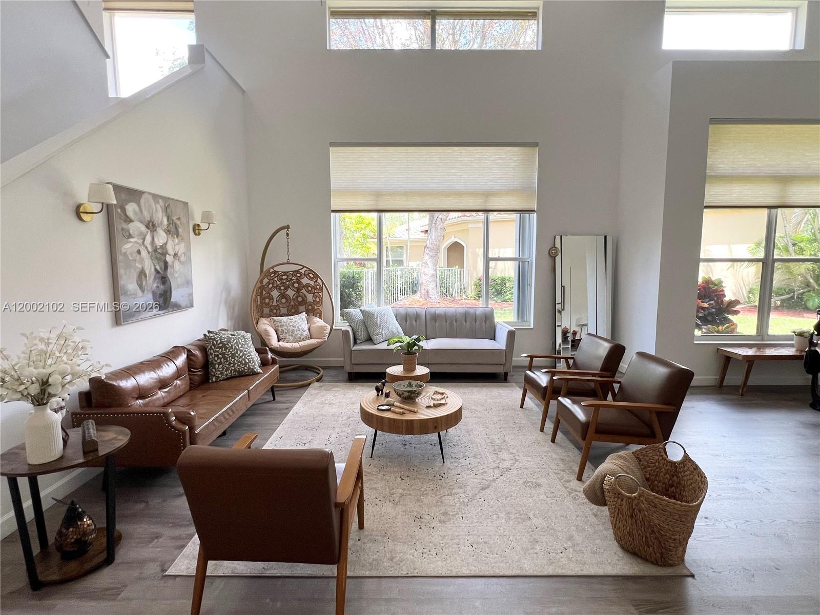 A bright living room features a leather sofa, armchairs, a hanging chair, and large windows — 2486 Bay Isle Dr, Weston FL 33327, WESTON, FL