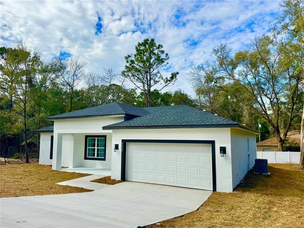 A single-story white house with a dark roof, a two-car garage, and a concrete driveway — 8428 N POCONO DRIVE, CITRUS SPRINGS, FL