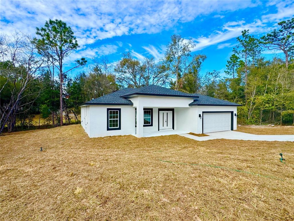 A white single-story house with a dark roof and a two-car garage sits on grass — 8428 N POCONO DRIVE, CITRUS SPRINGS, FL