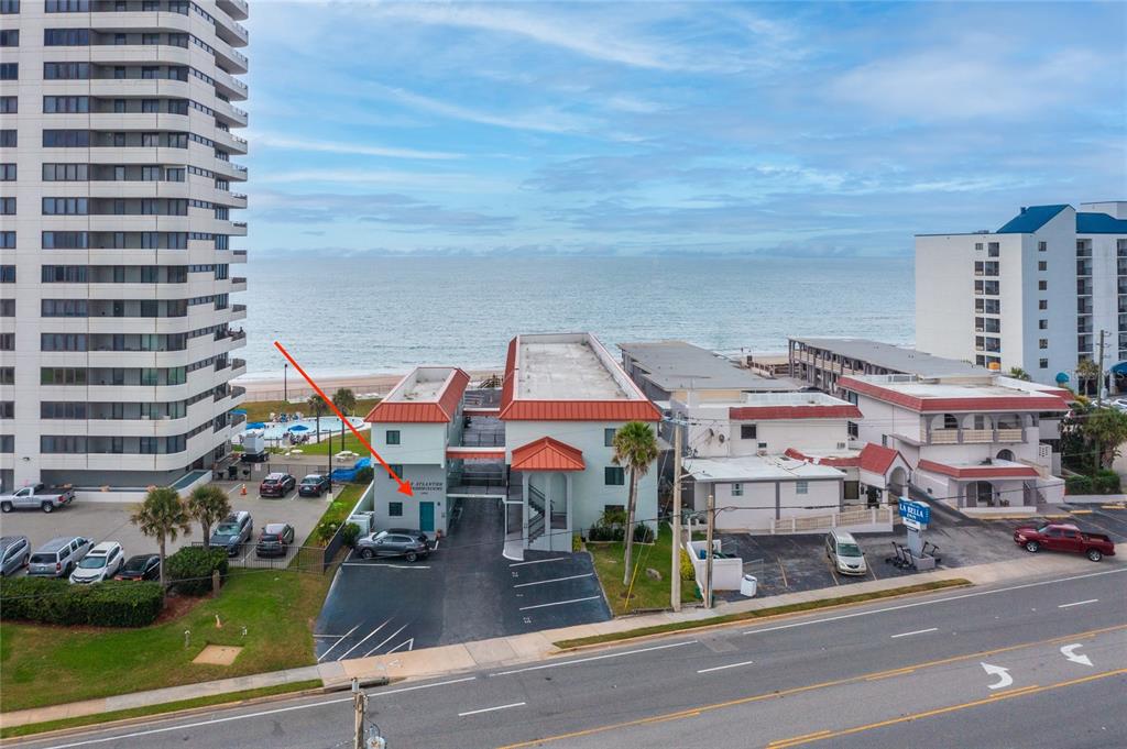 An aerial view shows a multi-story beachfront building with a red roof and parking lot — 1404 N ATLANTIC AVENUE UNIT 10, DAYTONA BEACH, FL