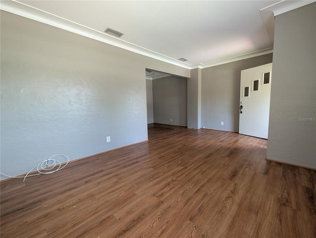 An empty living room features gray walls, wood-look flooring, and a white front door — 206 12TH AVENUE N, ST PETERSBURG, FL