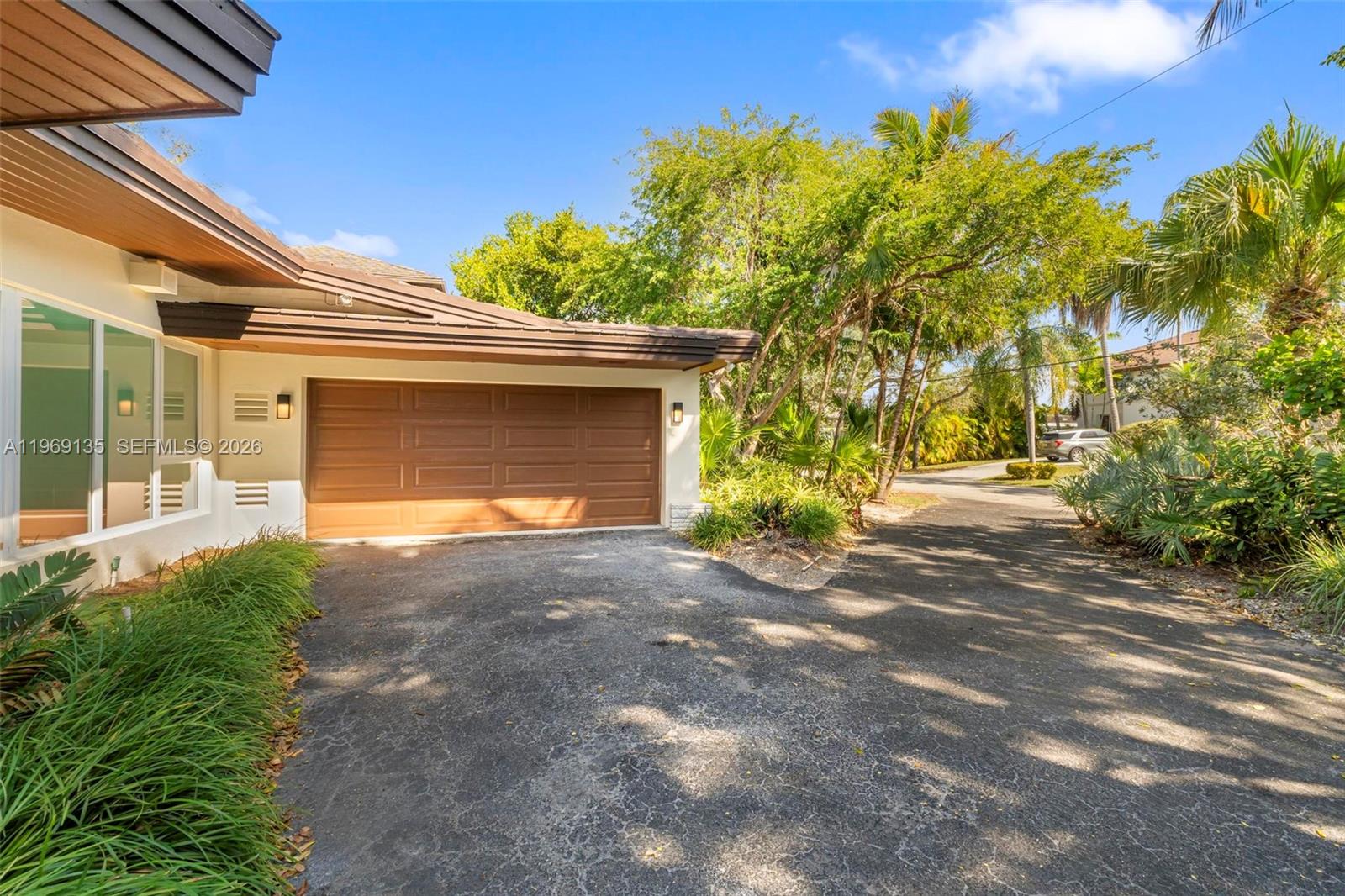 An asphalt driveway leads to a brown garage door attached to a house exterior — 13060 Lerida St, Coral Gables FL 33156, CORAL GABLES, FL