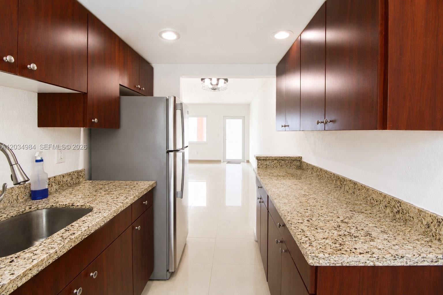 A galley kitchen features dark wood cabinets, granite countertops, and stainless steel appliances — 3550 SW 9th Ter # 8B, Miami FL 33135, MIAMI, FL