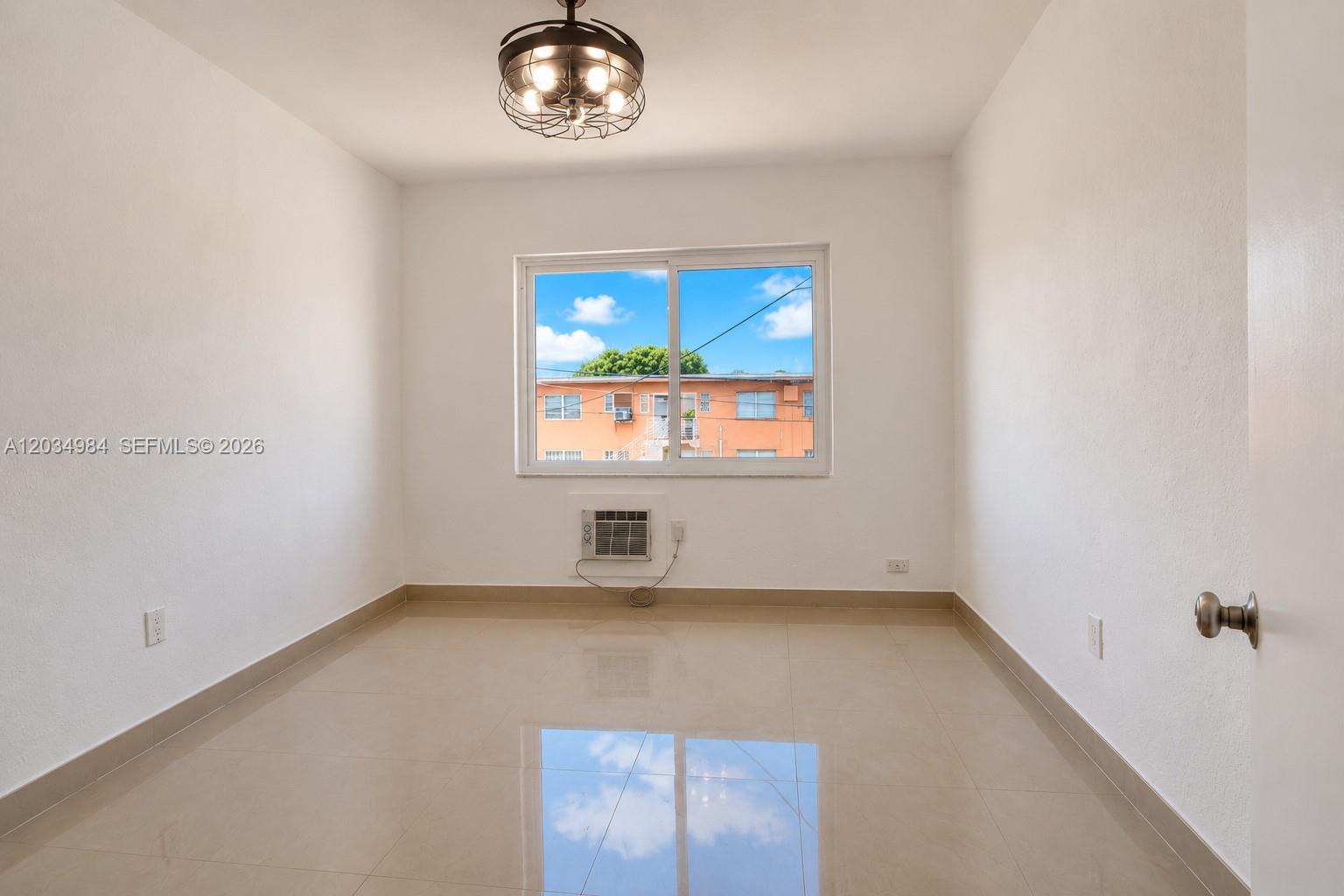 An empty room features white walls, beige tile flooring, a window, and a ceiling light — 3550 SW 9th Ter # 8B, Miami FL 33135, MIAMI, FL