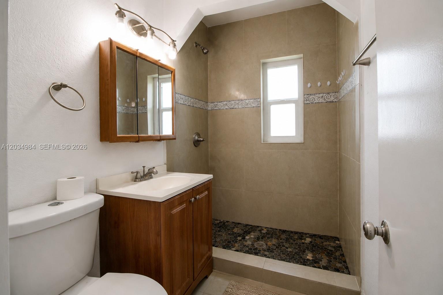 A bathroom features a wooden vanity, a toilet, and a walk-in shower with pebble flooring — 3550 SW 9th Ter # 8B, Miami FL 33135, MIAMI, FL