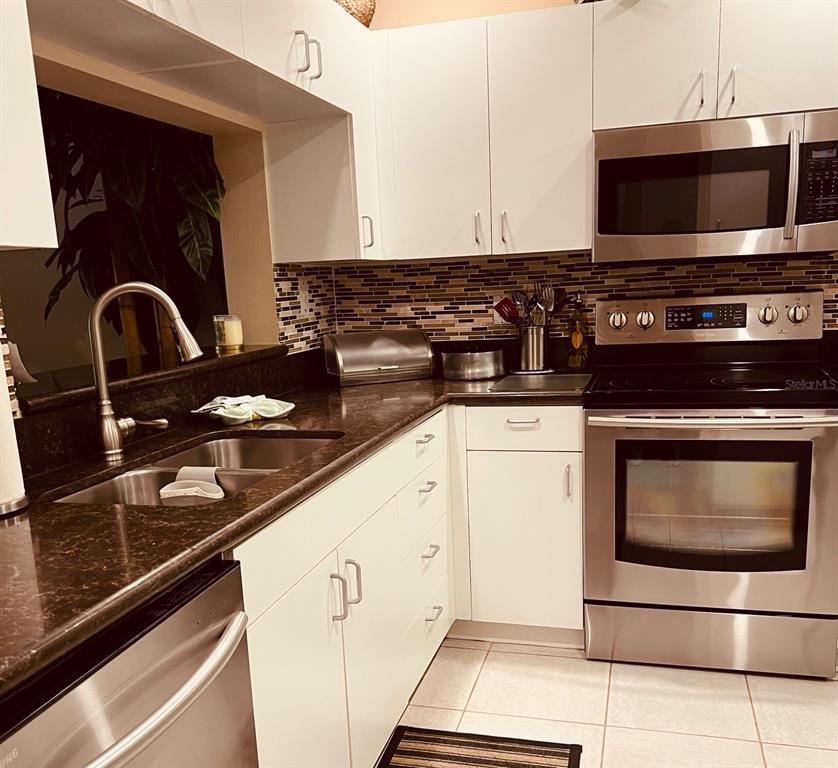 A kitchen features white cabinets, dark countertops, stainless steel appliances, and a tiled backsplash — 9620 CLUB SOUTH CIRCLE UNIT 5101, SARASOTA, FL