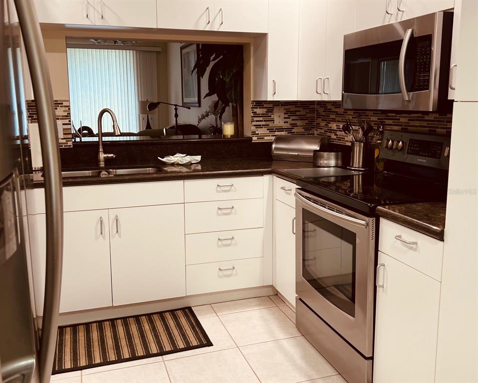 A kitchen features white cabinets, stainless steel appliances, dark countertops, and a tiled backsplash — 9620 CLUB SOUTH CIRCLE UNIT 5101, SARASOTA, FL