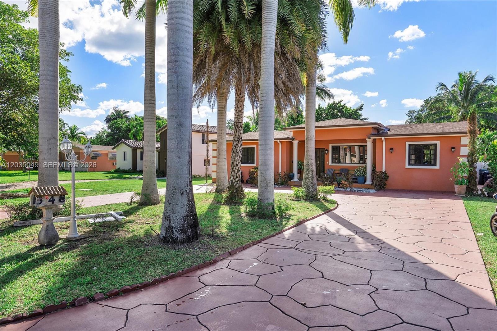 An orange house with a paved driveway and palm trees sits on a grassy lot — 348 NE 118th St, Miami FL 33161, MIAMI, FL